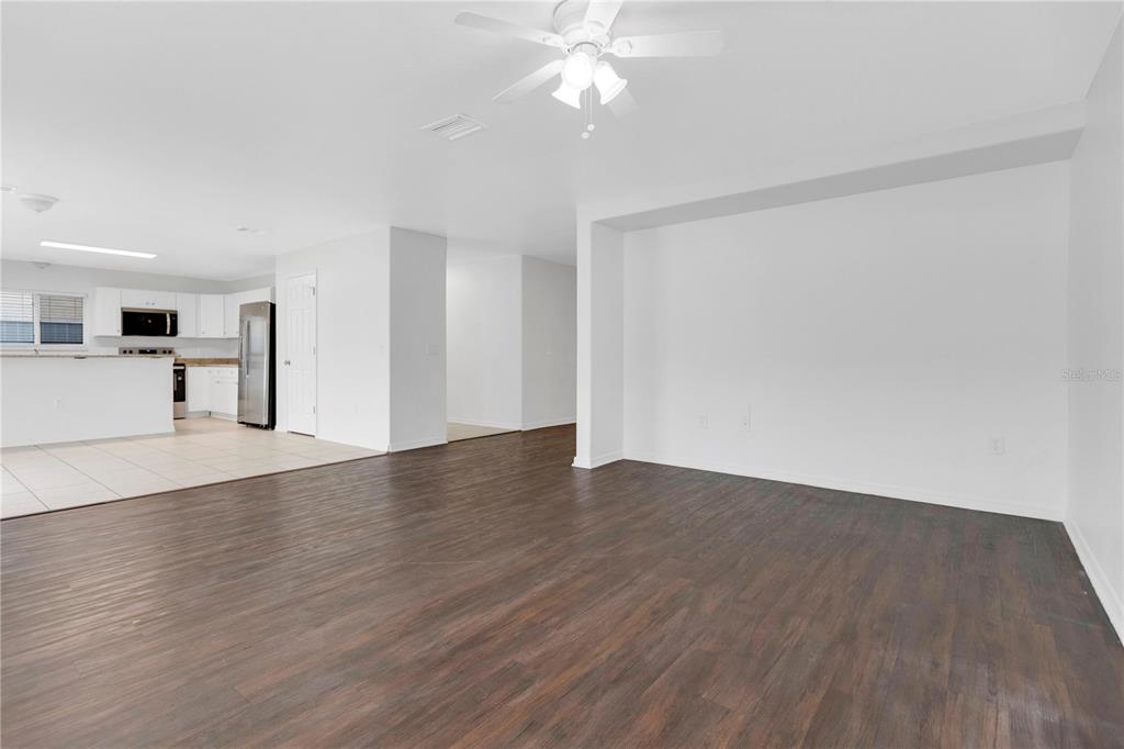 A living room with dark wood-look flooring opens to a kitchen with white cabinets — 10414 BOYETTE CREEK BOULEVARD, RIVERVIEW, FL