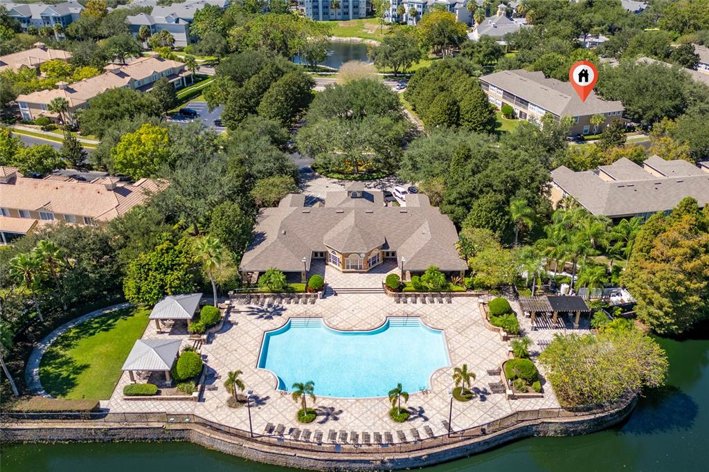 An aerial view shows a swimming pool and clubhouse surrounded by trees and a lake — 6422 AGASTIA COURT UNIT 101, ORLANDO, FL