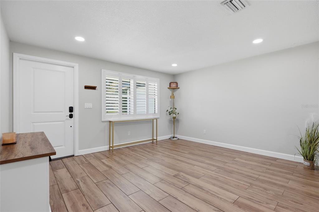 A bright room features light gray walls, wood-look tile flooring, a white door, and shutters — 6509 REED DRIVE, RIVERVIEW, FL