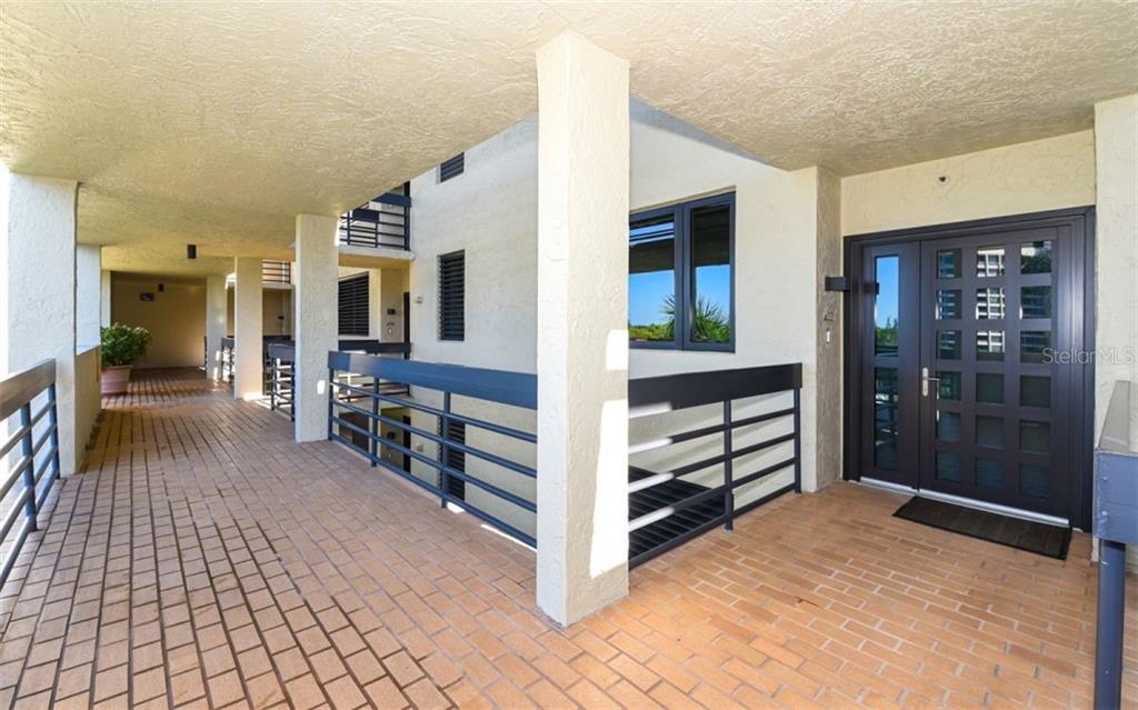 An outdoor walkway with brick flooring leads to a dark-framed glass front door — 1125 GULF OF MEXICO DRIVE UNIT 403, LONGBOAT KEY, FL