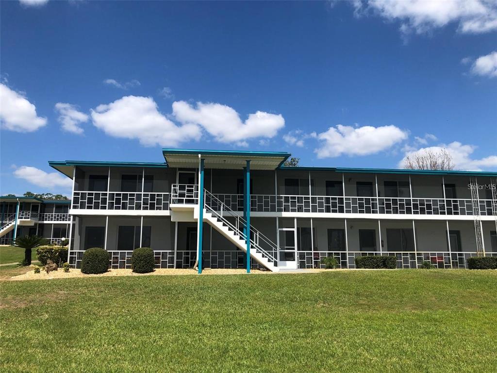 A two-story apartment building features a white exterior, blue trim, and an external staircase — 1600 W LAKE PARKER DRIVE UNIT A25, LAKELAND, FL