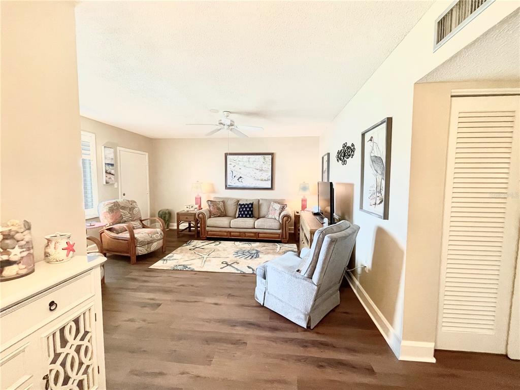 A living room features wood-look flooring, a sofa, two armchairs, and a coastal-themed area rug — 1600 W LAKE PARKER DRIVE UNIT A25, LAKELAND, FL