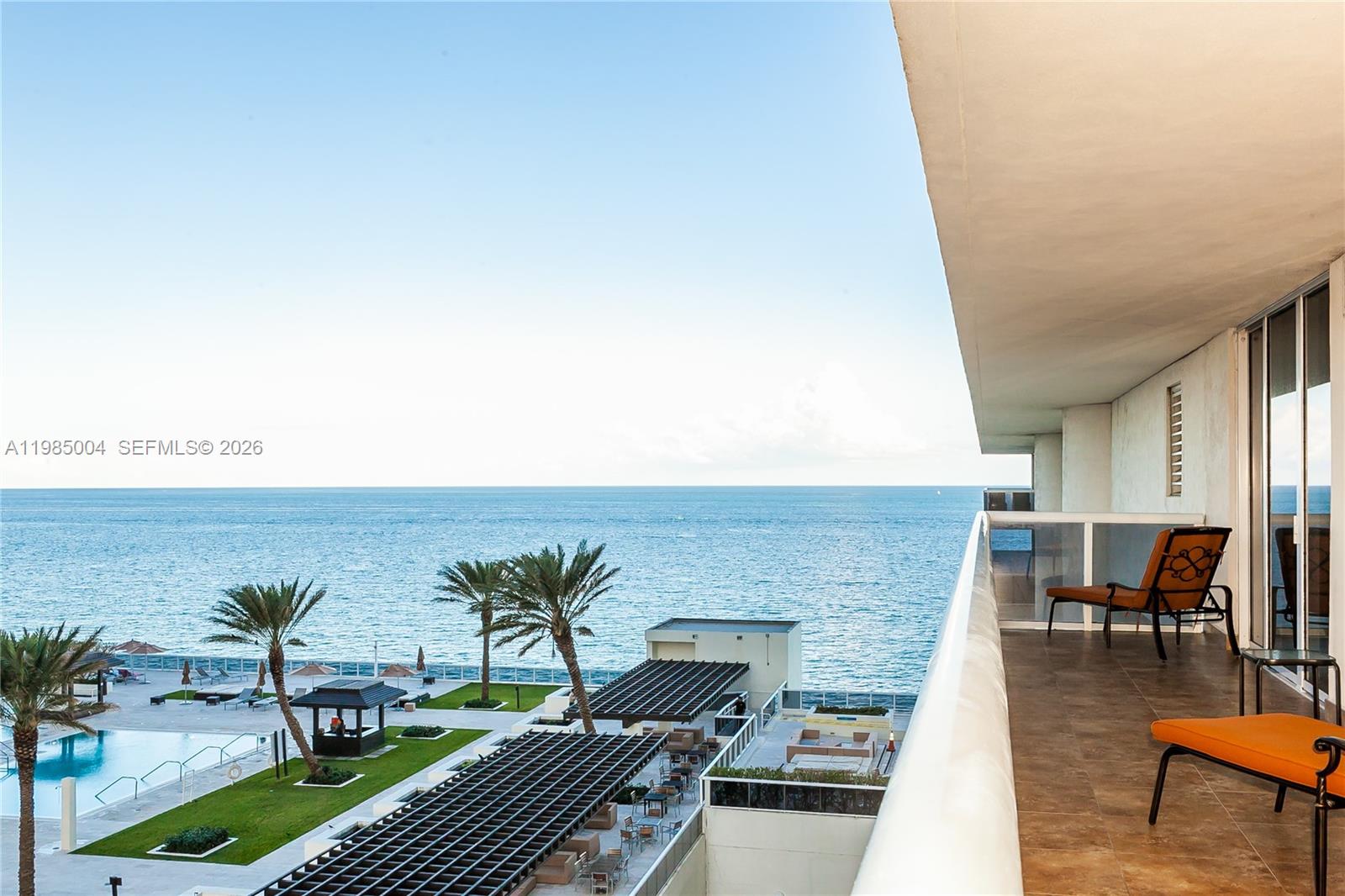 A balcony with orange chairs overlooks a swimming pool and the ocean — 1830 S Ocean Dr # 1108, Hallandale Beach FL 33009, HALLANDALE BEACH, FL