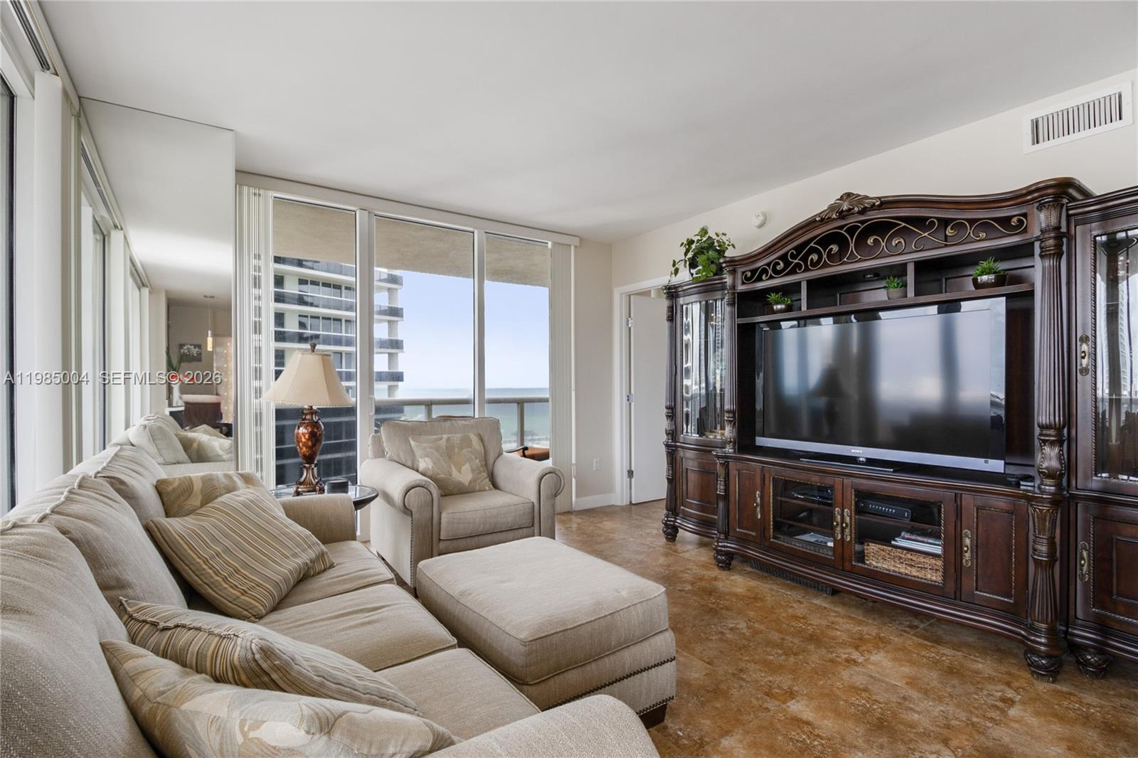 A living room features a large dark wood entertainment center, beige sofa, and ocean views — 1830 S Ocean Dr # 1108, Hallandale Beach FL 33009, HALLANDALE BEACH, FL