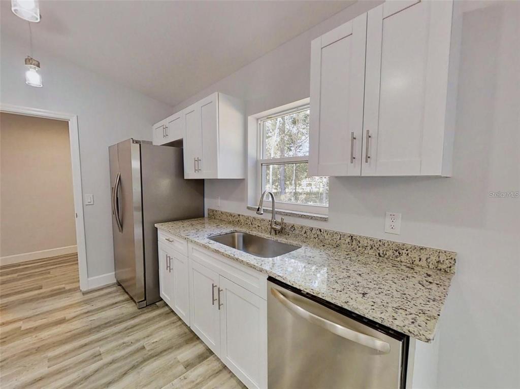 A kitchen features white cabinets, granite countertops, stainless steel appliances, and light wood-look flooring — 13163 SW 106TH PLACE, DUNNELLON, FL