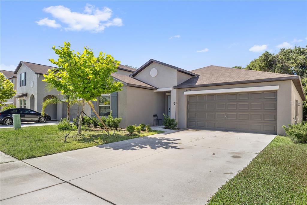 A single-story house with a beige stucco exterior, a brown roof, and a two-car garage — 4726 WILD SENNA BOULEVARD, TAMPA, FL