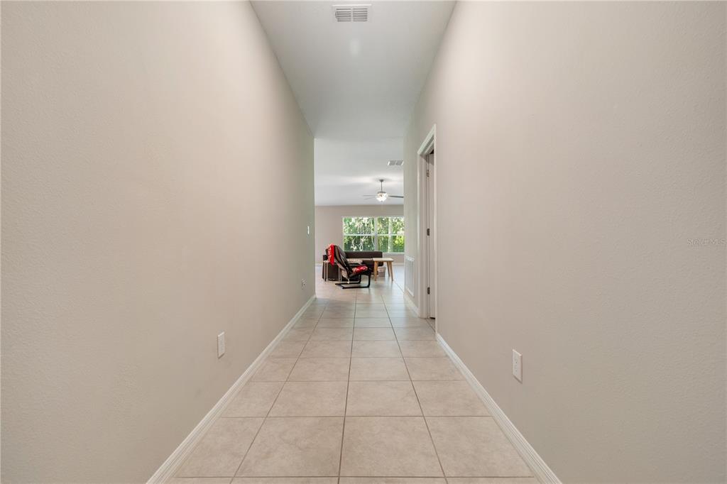 A tiled hallway leads from a neutral-walled corridor into a bright living area with windows — 4726 WILD SENNA BOULEVARD, TAMPA, FL