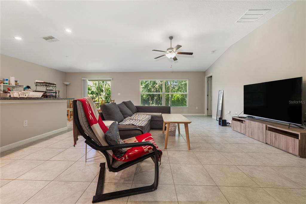A living room features light tile floors, a grey sectional sofa, and a large television — 4726 WILD SENNA BOULEVARD, TAMPA, FL