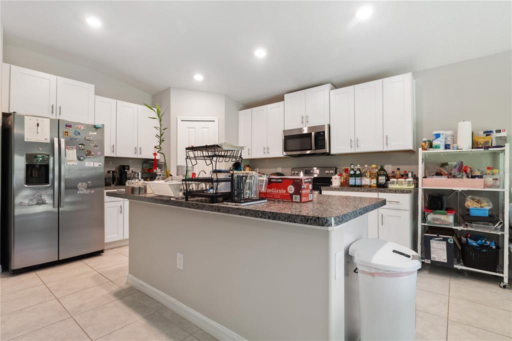 A kitchen features white cabinets, granite countertops, a center island, and stainless steel appliances — 4726 WILD SENNA BOULEVARD, TAMPA, FL