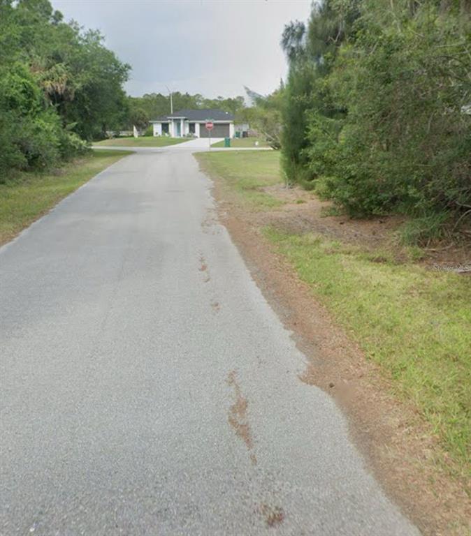A paved road leads toward a single-story house with a garage and a stop sign — 23350 BUCKNER AVENUE, PUNTA GORDA, FL