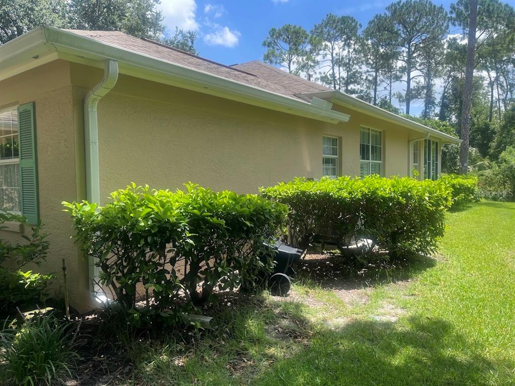 The exterior side of a tan stucco house features green shutters, white gutters, and landscaping — 16 LAFAYETTE LANE, PALM COAST, FL