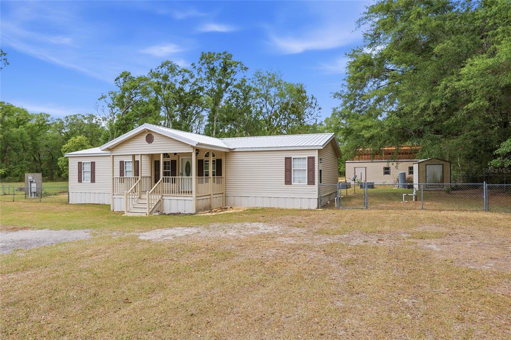 A beige manufactured home with a front porch sits on a grassy lot with trees — 9528 NW 235TH TERRACE, ALACHUA, FL
