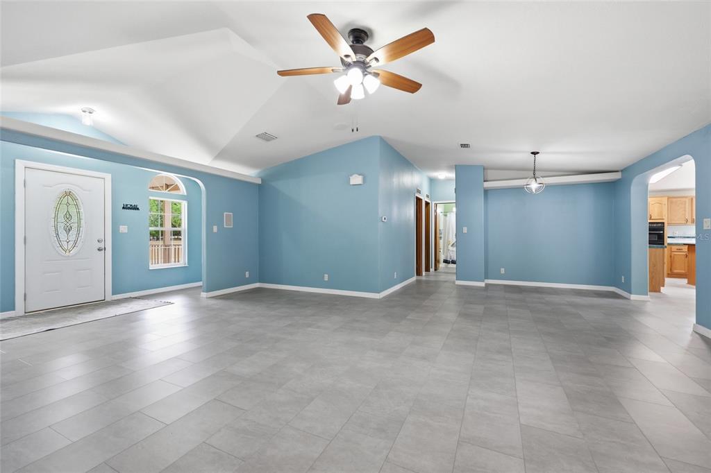 A spacious living area with light blue walls, gray tile flooring, and a vaulted ceiling — 9528 NW 235TH TERRACE, ALACHUA, FL