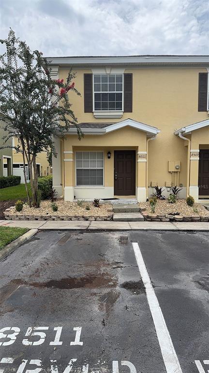 A two-story yellow townhouse exterior with a brown front door and a small landscaped garden — 8511 TRAIL WIND DRIVE, TAMPA, FL