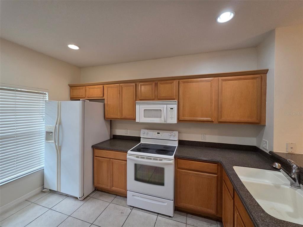 A kitchen features wooden cabinets, white appliances, dark countertops, and tile flooring — 8511 TRAIL WIND DRIVE, TAMPA, FL