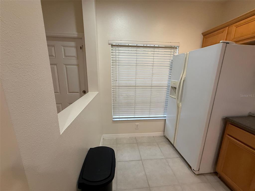 A kitchen corner features a white refrigerator, a window with blinds, and tiled flooring — 8511 TRAIL WIND DRIVE, TAMPA, FL
