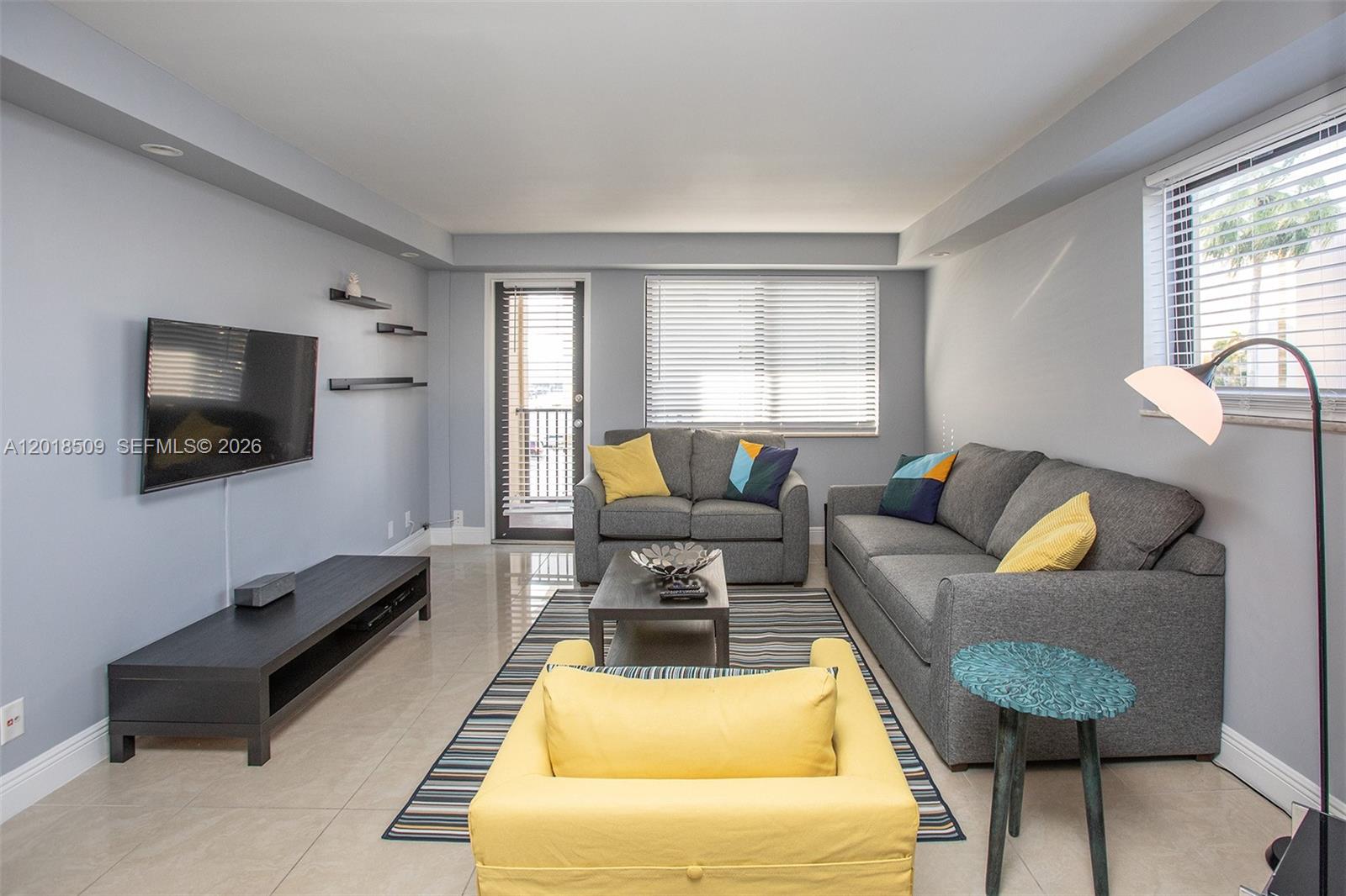 A living room features gray walls, tile flooring, a gray sofa, and a yellow armchair — HALLANDALE BEACH, FL