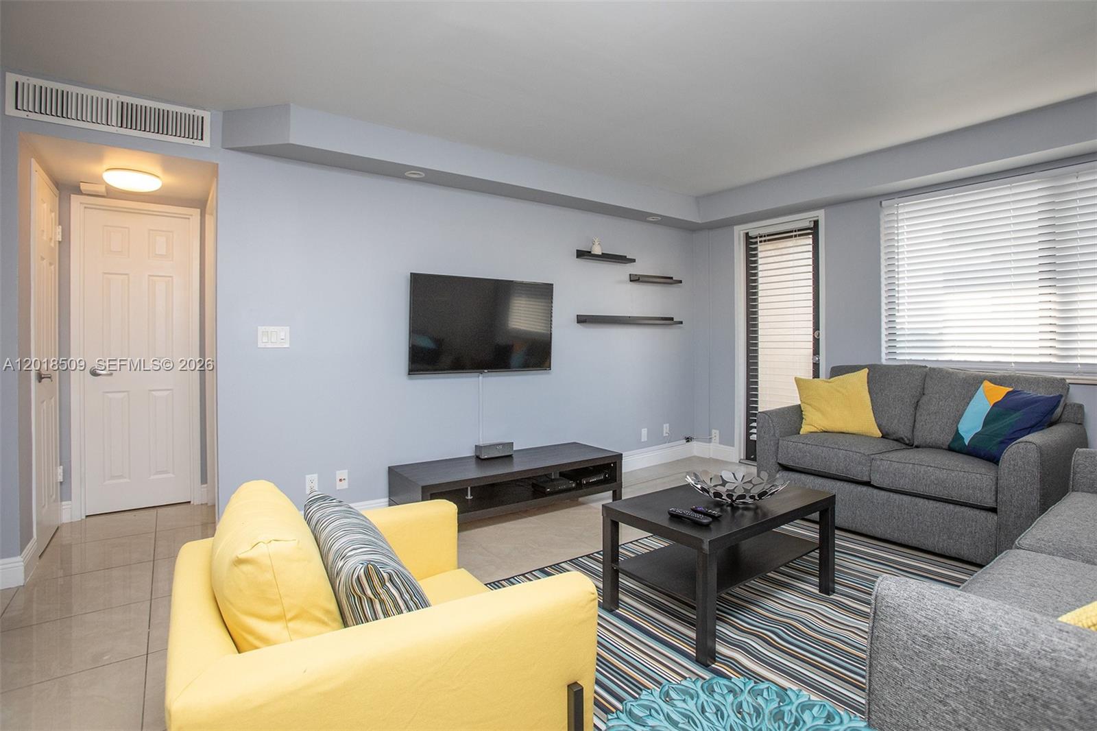 A living room features light blue walls, a gray sofa, a yellow armchair, and tile flooring — HALLANDALE BEACH, FL