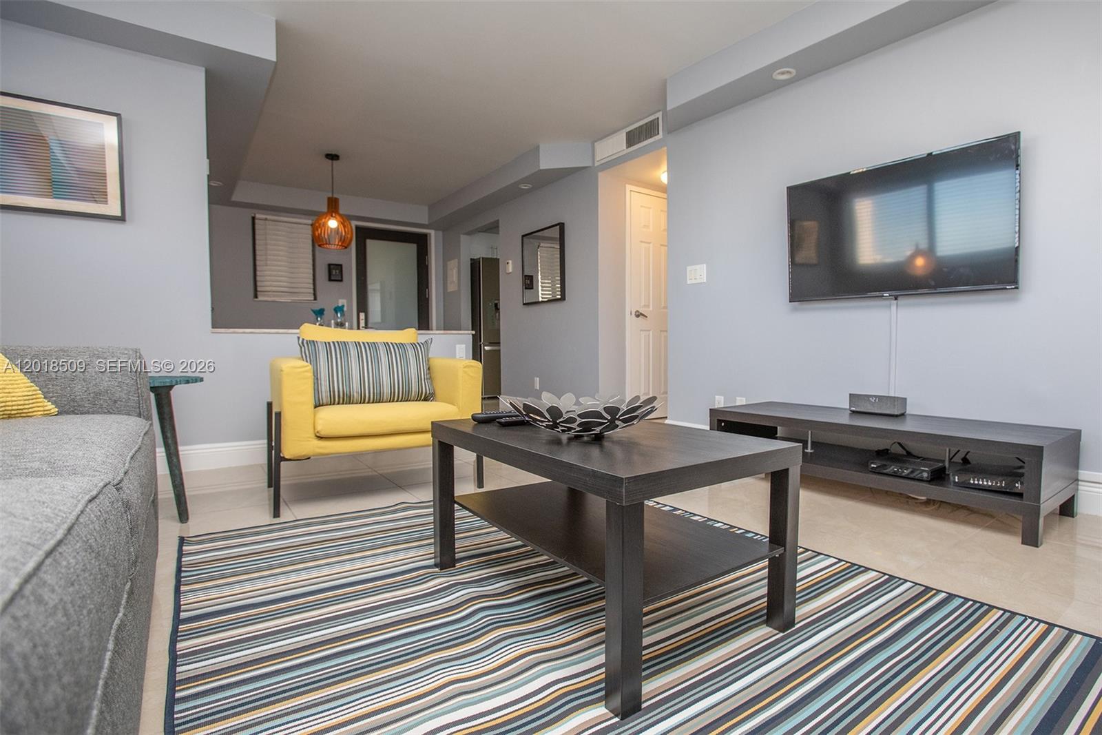 A living room features a grey sofa, a yellow armchair, a coffee table, and a television — HALLANDALE BEACH, FL