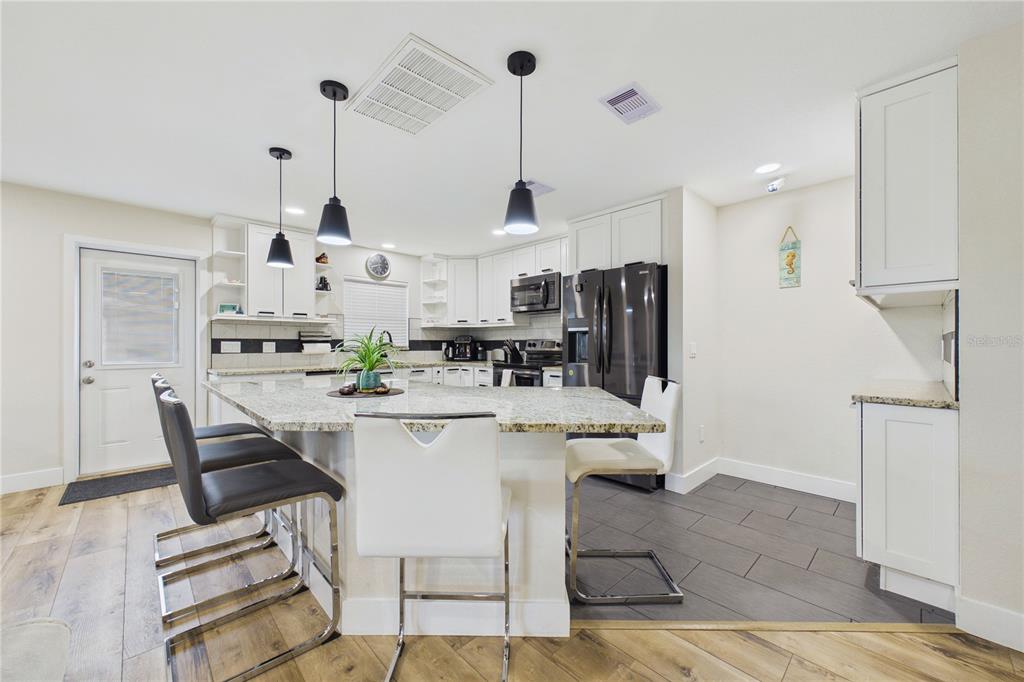 A kitchen features white cabinets, granite countertops, a central island, and stainless steel appliances — 132 CONCORD DRIVE NE, PORT CHARLOTTE, FL