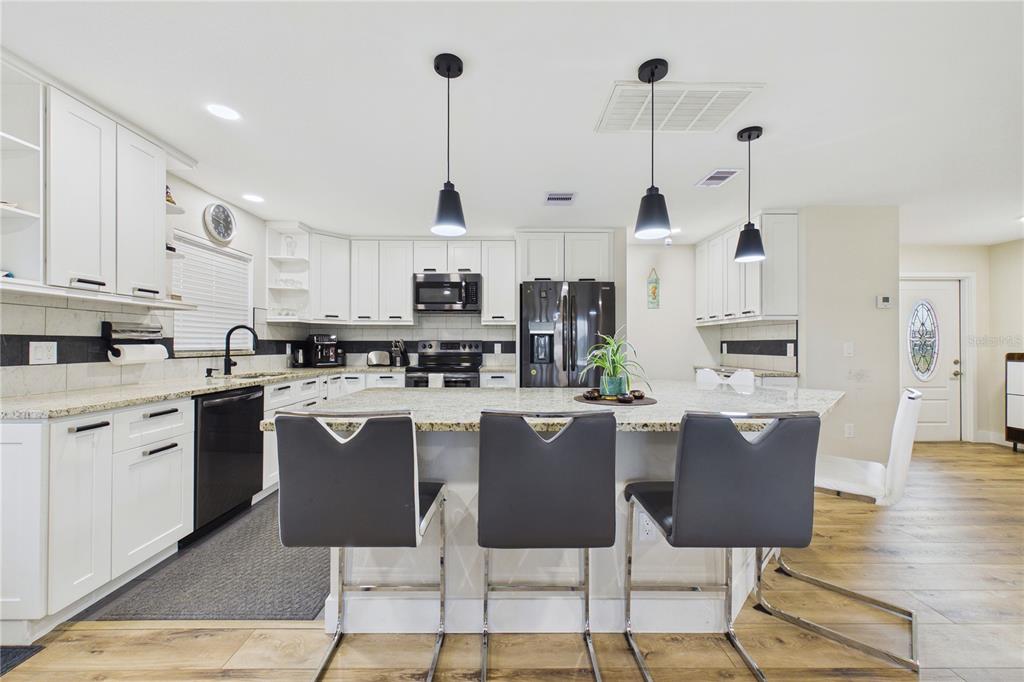 A modern kitchen features white cabinets, granite countertops, a central island, and three bar stools — 132 CONCORD DRIVE NE, PORT CHARLOTTE, FL