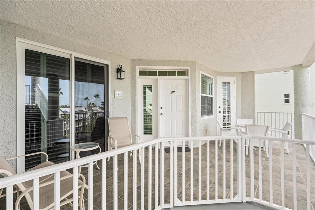 A balcony features tiled flooring, white railings, outdoor furniture, and sliding glass doors — 1260 DOLPHIN BAY WAY UNIT 404, SARASOTA, FL