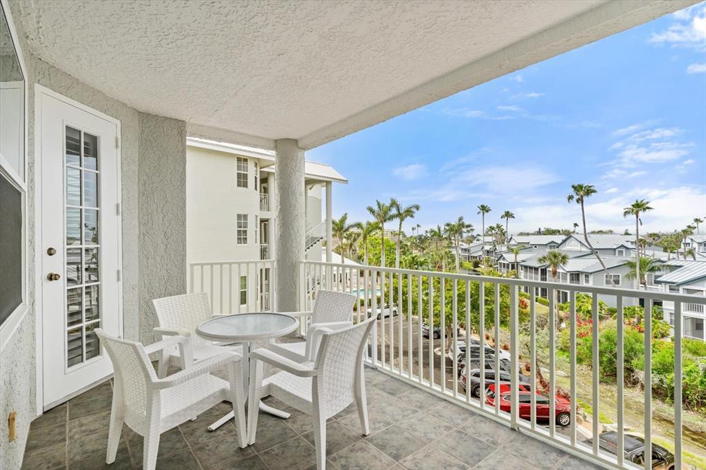 A balcony with a small table and four chairs overlooks a parking lot and buildings — 1260 DOLPHIN BAY WAY UNIT 404, SARASOTA, FL
