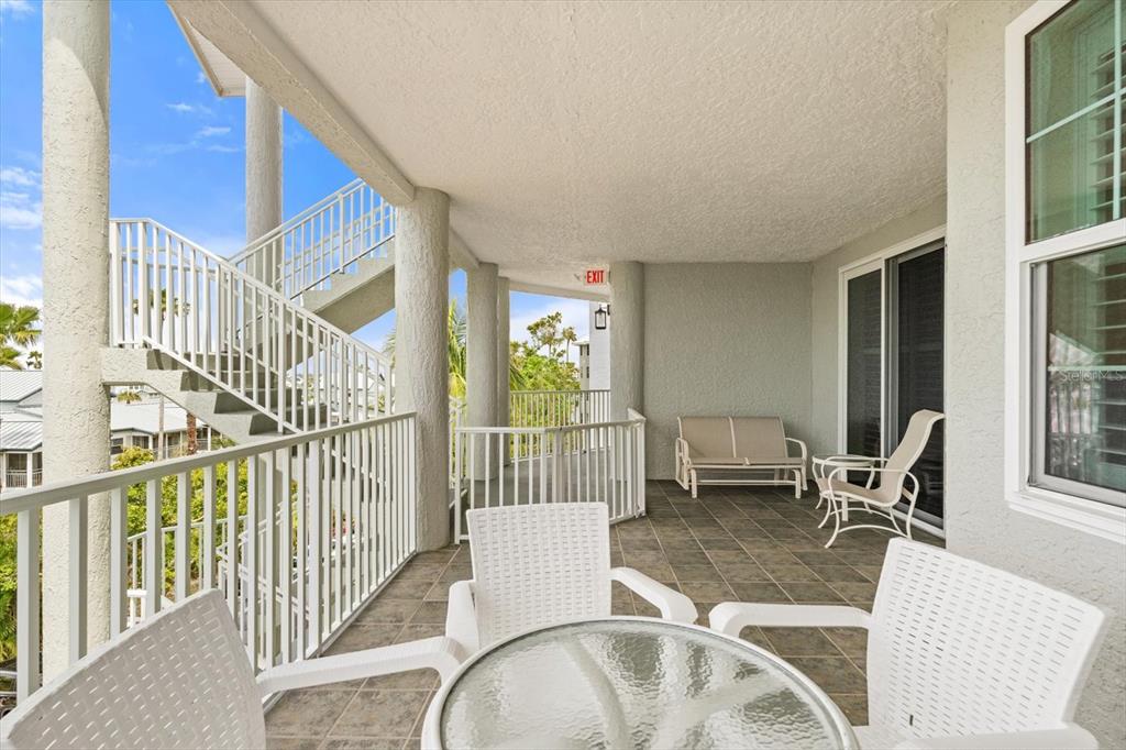 A covered balcony features white railings, tiled flooring, outdoor furniture, and an exterior staircase — 1260 DOLPHIN BAY WAY UNIT 404, SARASOTA, FL