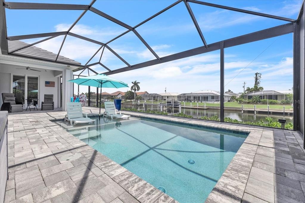 A screened-in patio features a rectangular swimming pool with a tanning ledge and canal views — 630 CORONADO DRIVE, PUNTA GORDA, FL