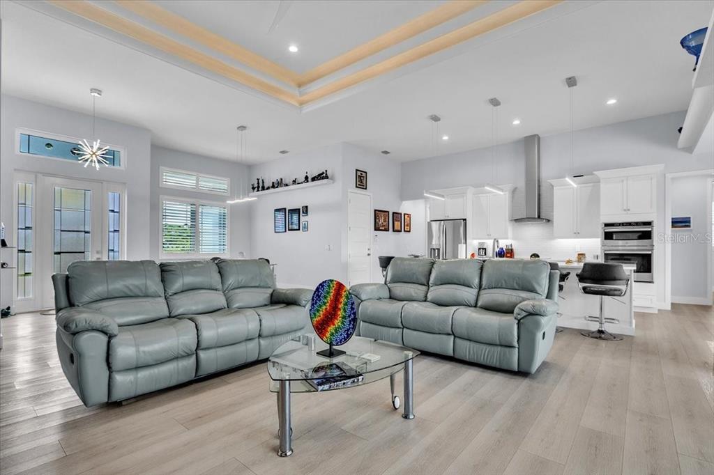 An open-concept living room and kitchen featuring gray leather sofas, light wood flooring, and cabinetry — 630 CORONADO DRIVE, PUNTA GORDA, FL