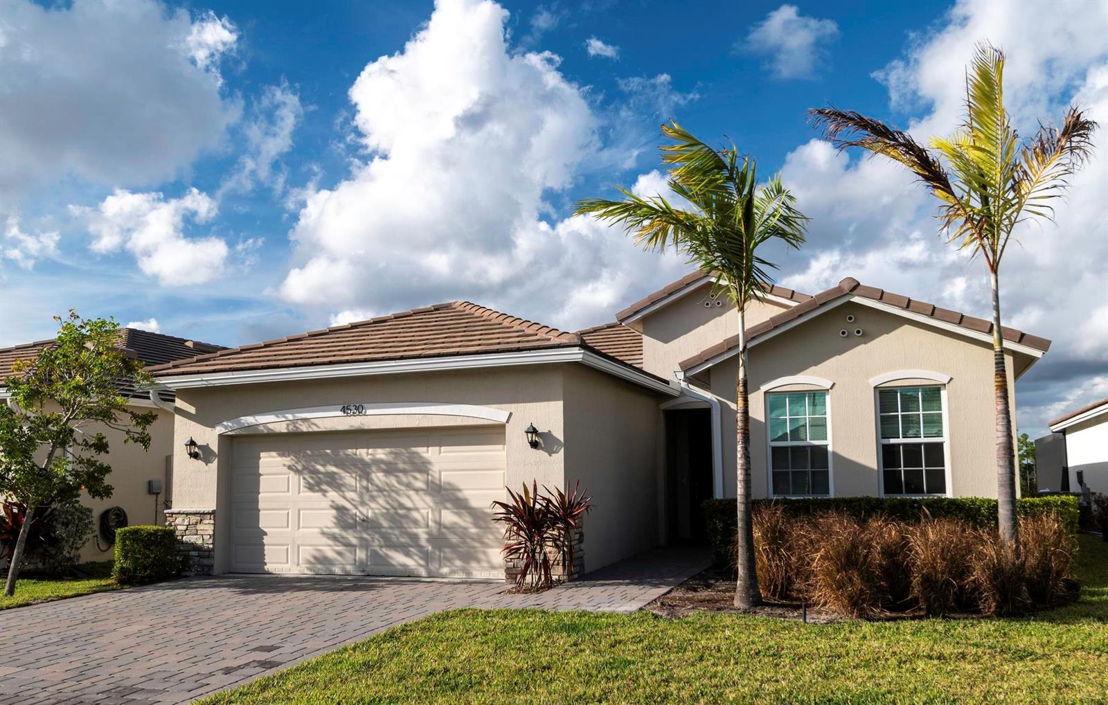 A single-story suburban house with a tan stucco exterior, a two-car garage, and palm trees — 4530 NW Exchange Avenue, Jensen Beach FL 34957, JENSEN BEACH, FL