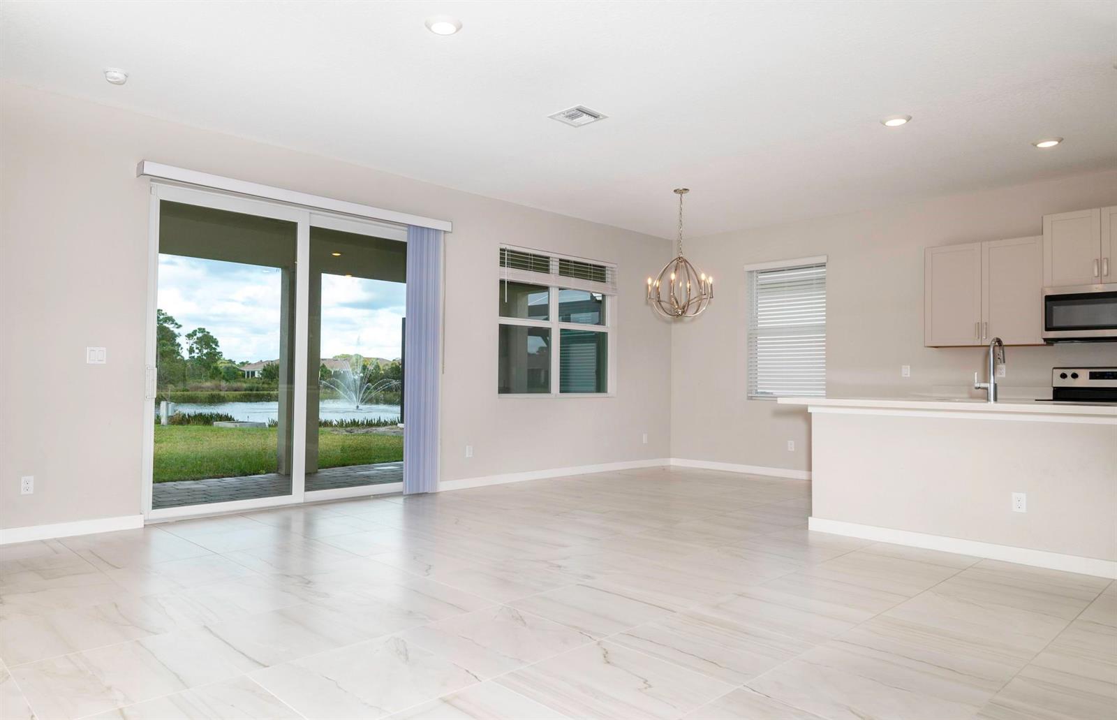 An open-concept dining area with tile floors, a chandelier, and sliding doors overlooking a pond — 4530 NW Exchange Avenue, Jensen Beach FL 34957, JENSEN BEACH, FL