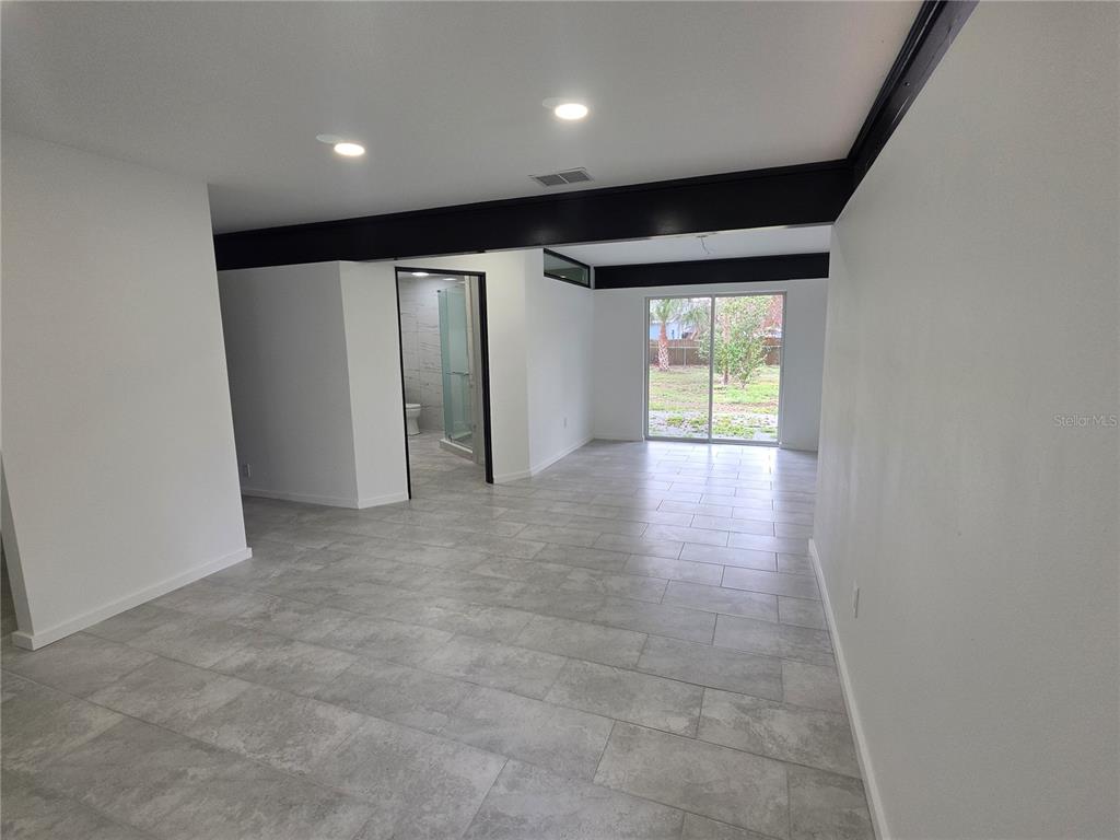A bright room with gray tile flooring, a black ceiling beam, and a sliding glass door — 1390 S SWEARINGEN, BARTOW, FL