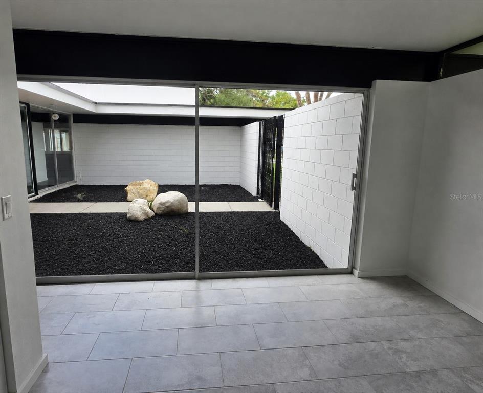 A room with gray tile flooring looks out through sliding glass doors onto a walled courtyard — 1390 S SWEARINGEN, BARTOW, FL