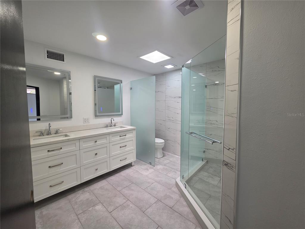 A modern bathroom features a double vanity, a glass-enclosed shower, and a private toilet area — 1390 S SWEARINGEN, BARTOW, FL