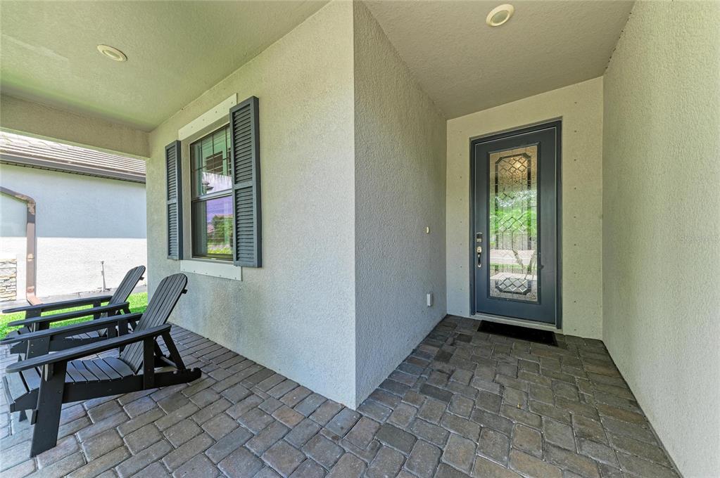 A covered front porch features a paver floor, two black chairs, and a glass-paneled door — 11515 SWEETGRASS DRIVE, BRADENTON, FL