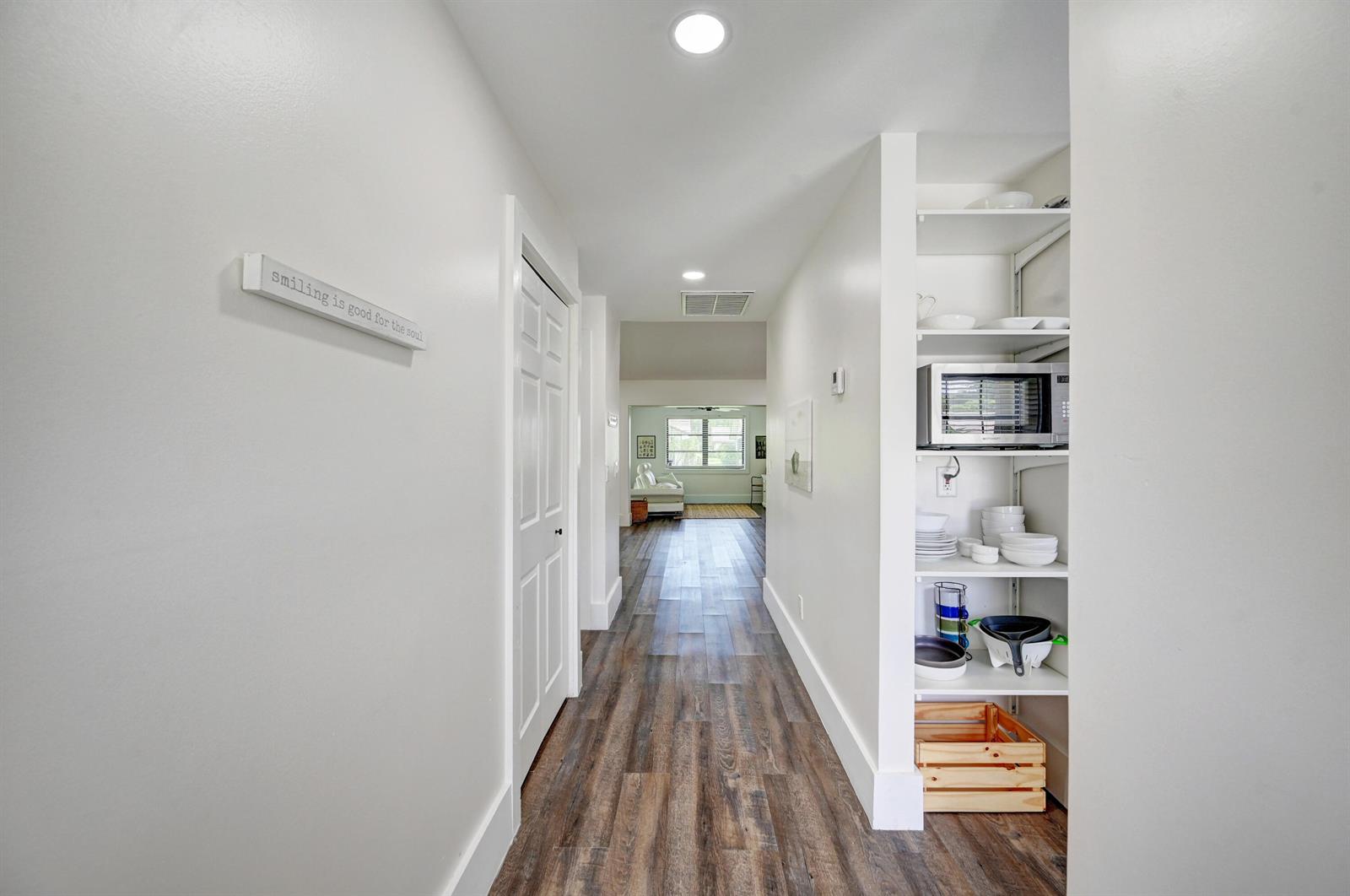 A hallway with wood-look flooring leads to a living area, featuring built-in open shelving — 2756 Carnation Court, Delray Beach FL 33445, DELRAY BEACH, FL