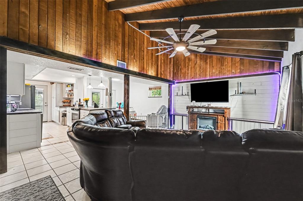 A living room with wood-paneled walls, exposed ceiling beams, a ceiling fan, and a fireplace — 7238 HILLCREST STREET, LEESBURG, FL