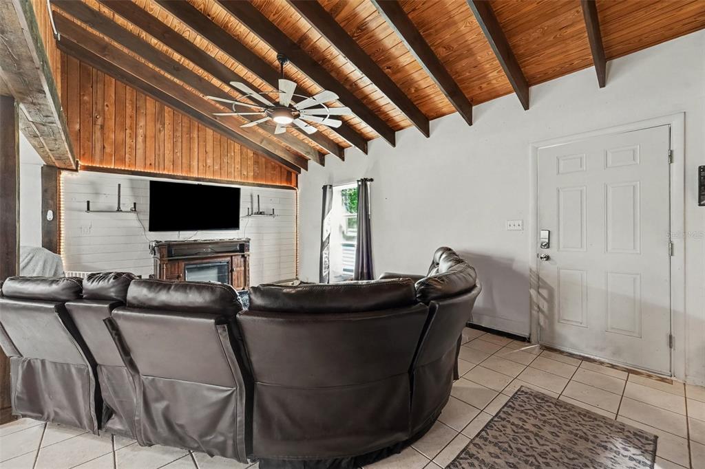 A living room features a vaulted wood-paneled ceiling, exposed beams, and a large leather sectional — 7238 HILLCREST STREET, LEESBURG, FL
