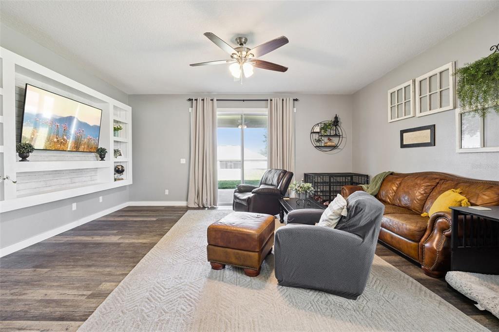 A living room features a built-in media center, leather furniture, and sliding glass patio doors — 11531 ARBOR GATE DRIVE, CLERMONT, FL