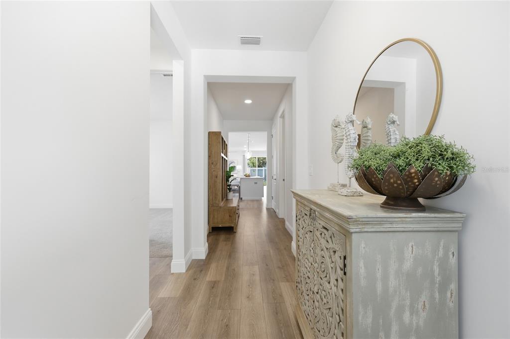 A hallway with wood-look flooring leads to an open kitchen area past a decorative cabinet — 144 POINT PLEASANT DRIVE, PALM COAST, FL