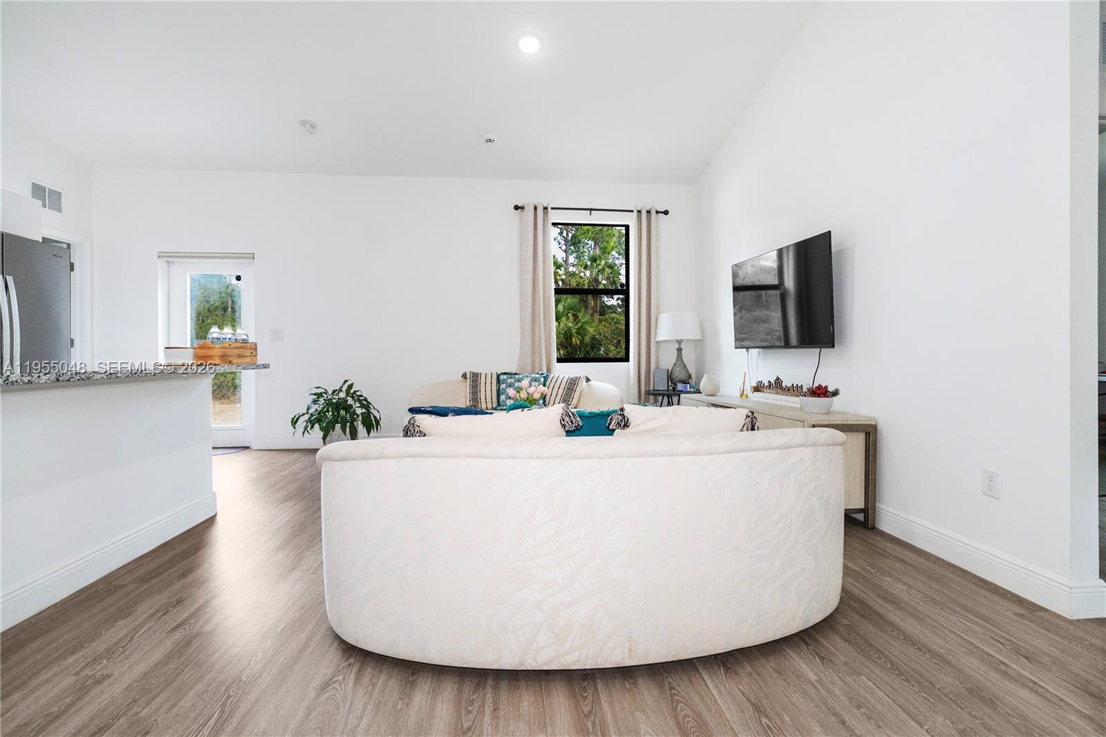 A living room features a curved sofa, wood-look flooring, and a wall-mounted television — 8031 Sandy Cir, La Belle FL 33935, LA BELLE, FL