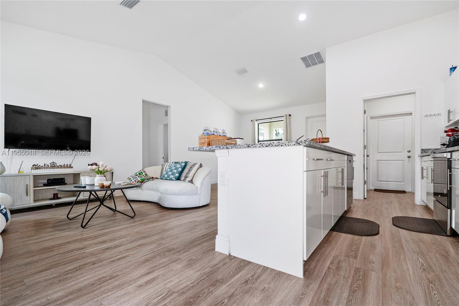 An open-concept living room and kitchen feature white cabinetry, granite countertops, and wood-look flooring — 8031 Sandy Cir, La Belle FL 33935, LA BELLE, FL