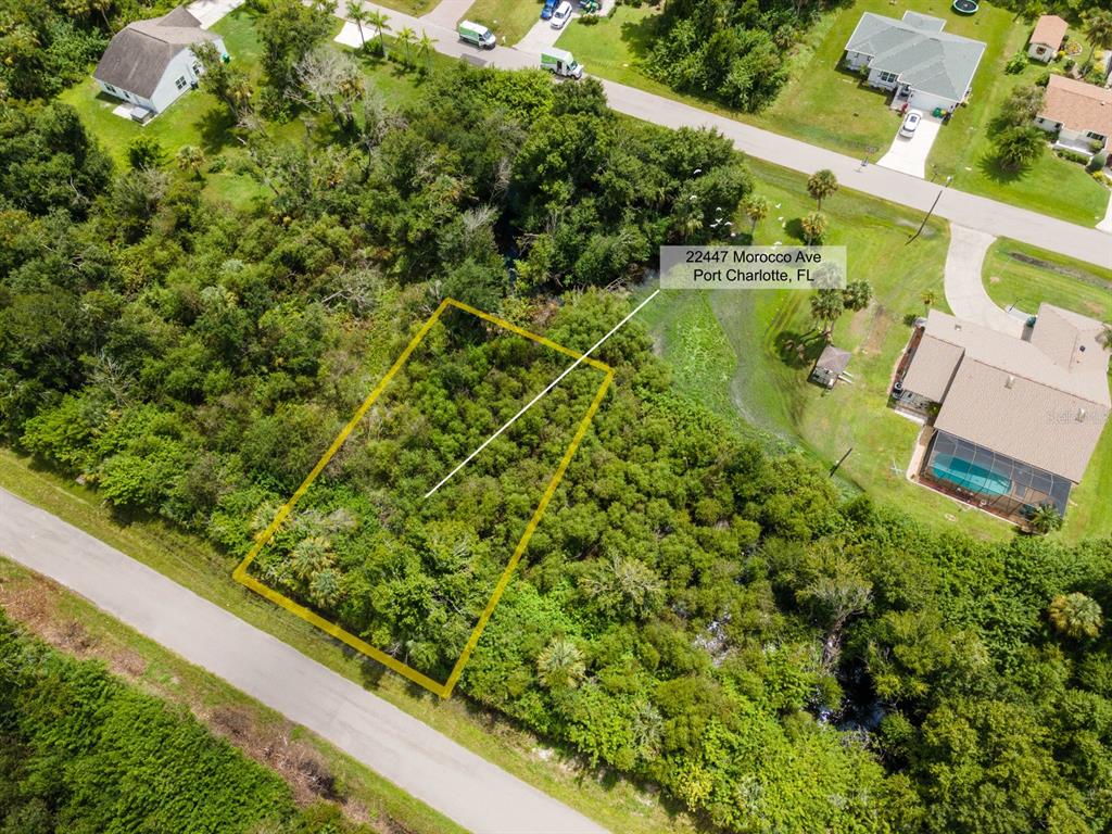 An aerial view shows a rectangular, wooded vacant lot outlined in yellow near a road — 22447 MOROCCO AVENUE, PORT CHARLOTTE, FL