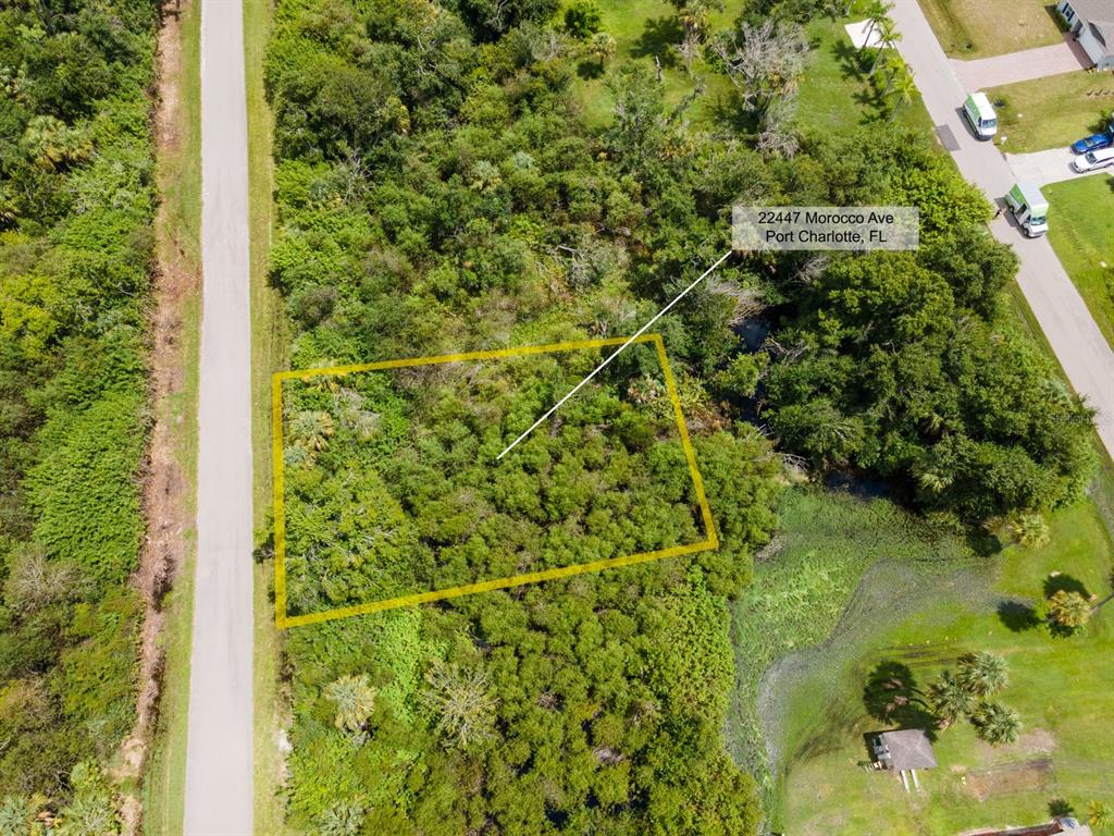 An aerial view shows a rectangular vacant lot outlined in yellow amidst dense green vegetation — 22447 MOROCCO AVENUE, PORT CHARLOTTE, FL