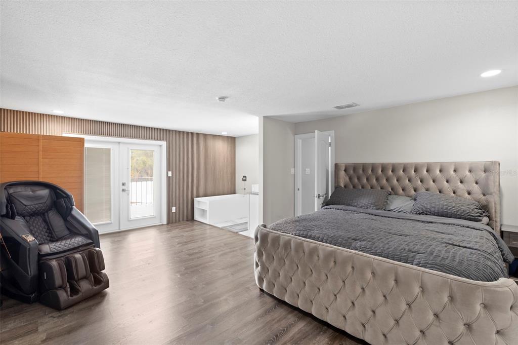 A bedroom features a tufted bed, a massage chair, wood-slat walls, and an open-concept bathtub — 10525 HOMESTEAD DRIVE, TAMPA, FL