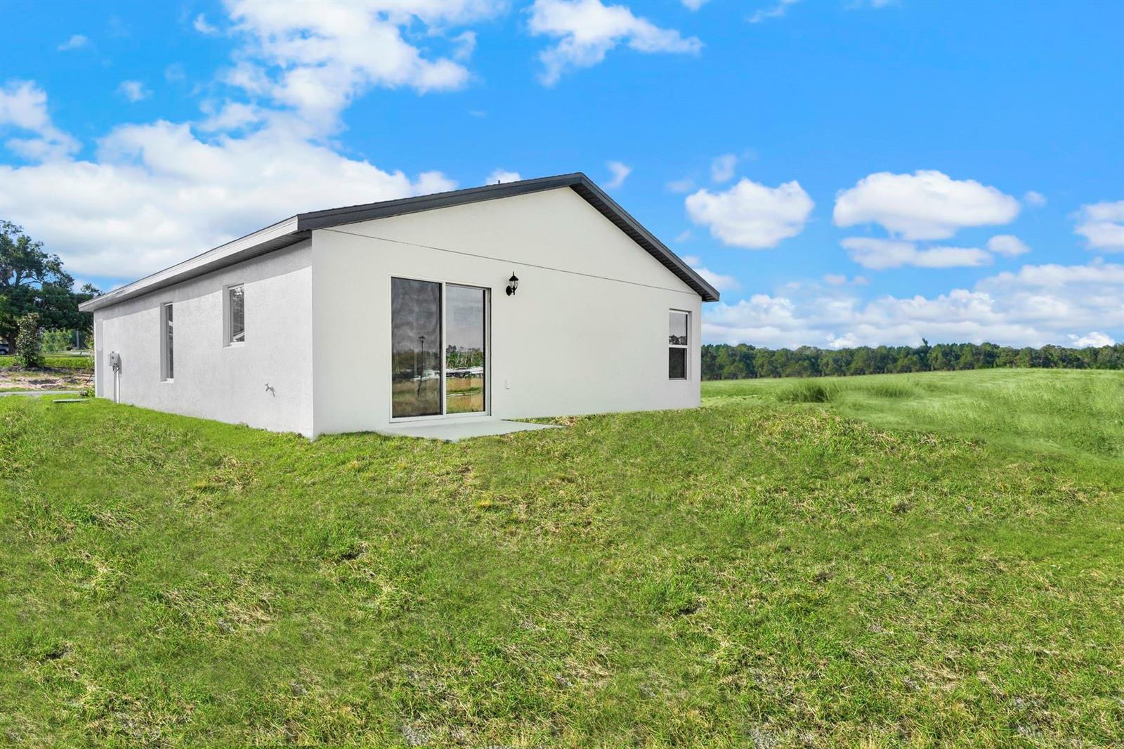 The exterior of a white, single-story house sits on a grassy hill under a blue sky — 8556 105th Avenue, Vero Beach FL 32967, VERO BEACH, FL