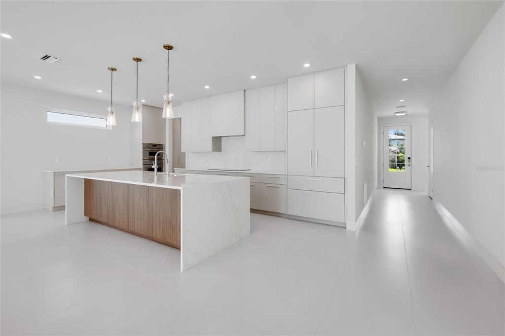A modern kitchen features white cabinetry, a waterfall island with wood paneling, and pendant lighting — 2596 FLOYD STREET, SARASOTA, FL
