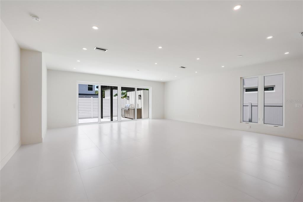 A bright, empty room features white tile floors, recessed lighting, and large sliding glass doors — 2596 FLOYD STREET, SARASOTA, FL