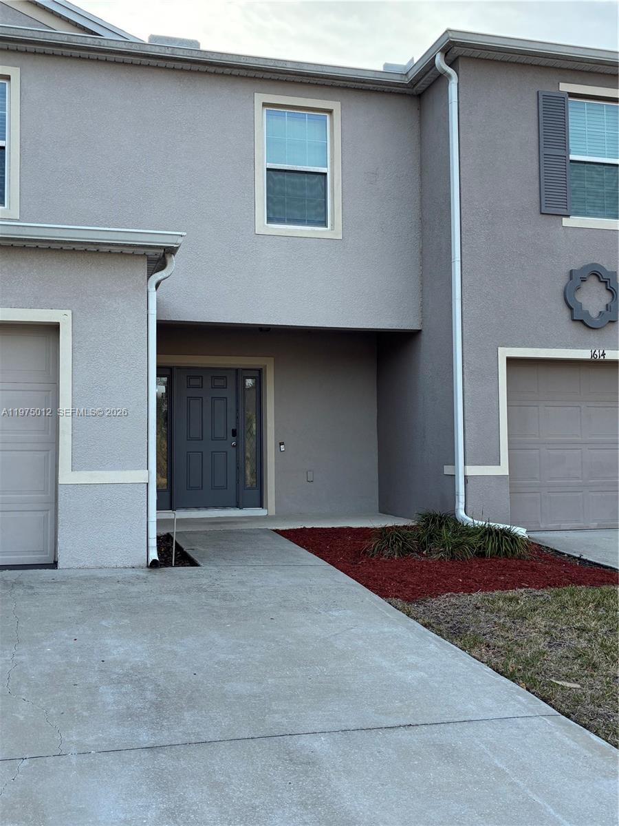 A two-story townhouse exterior features a gray stucco facade, two garage doors, and a walkway — 1612 Primo Ct, Daytona FL 32117, DAYTONA, FL